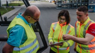 Kolm ohutusvestidega inimest vestlevad: Ohutuskonsultatsioon kliendi ruumides kohapeal. Kolm ohutusvestidega inimest vestlevad: Ohutuskonsultatsioon kliendi ruumides kohapeal.