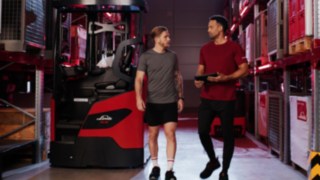 Kaks spordirõivastes inimest seisavad Linde MH lükandmastiga virnastaja Ri16 ees; üks neist hoiab käes tahvelarvutit.